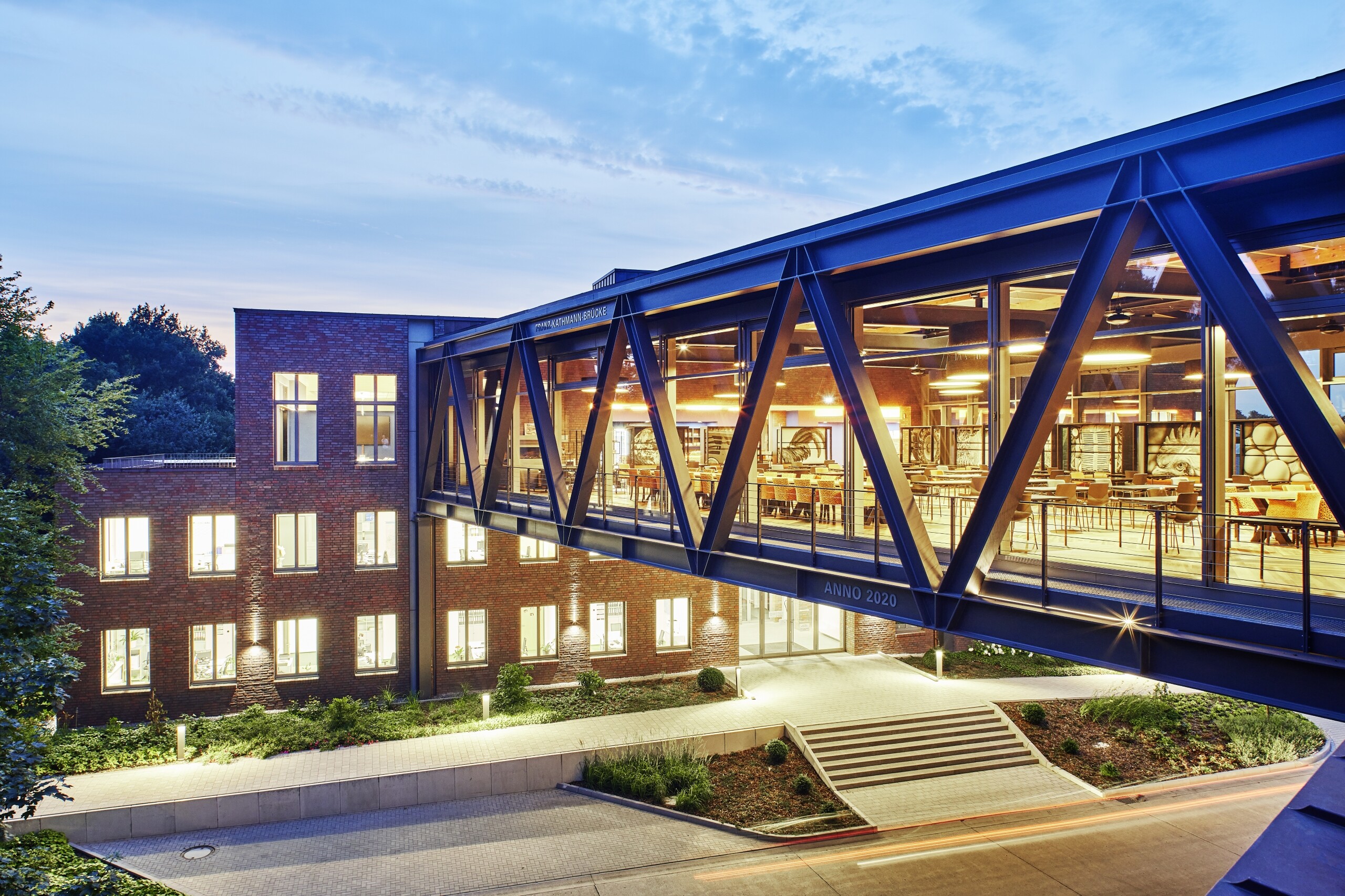 Verwaltungsgebäude von Big Dutchman in Calveslage mit verglaster Verbindungsbrücke, entworfen von Geising + Böker Architekten – moderne Büroarchitektur bei Abendlicht.